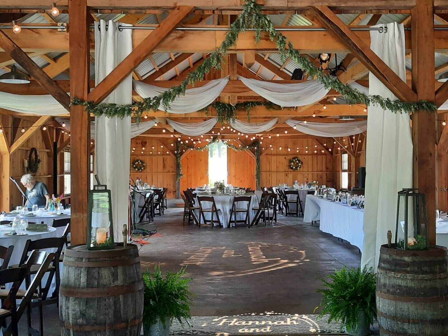 Rustic barn venue decorated for a wedding reception with draped fabric and greenery.