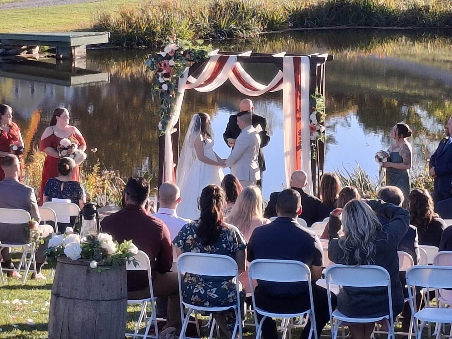 Couple sharing a kiss during an outdoor wedding ceremony by a lake.