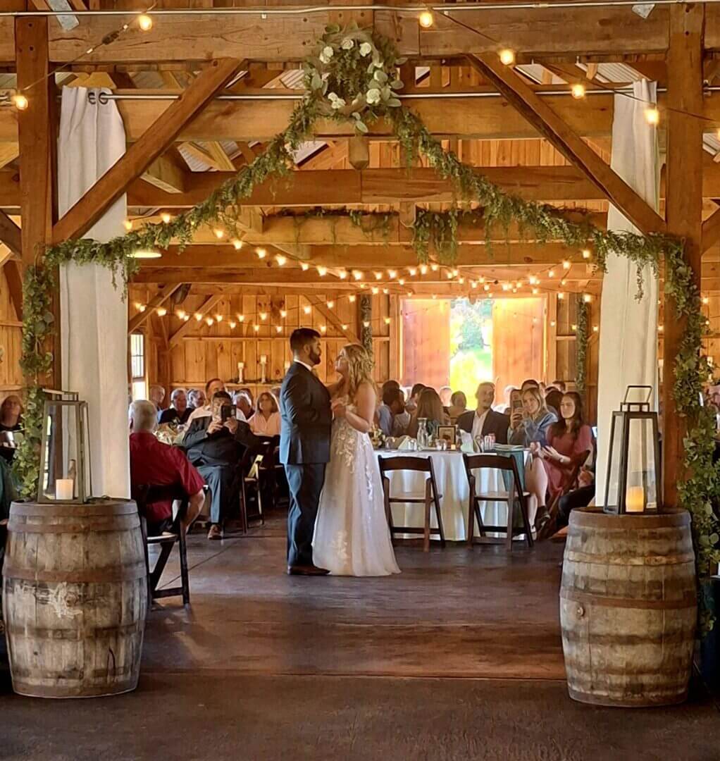 Bride and groom share first dance in a warmly lit rustic barn venue.